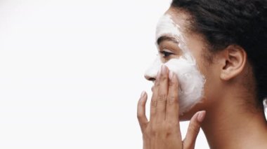 Afro-Amerikalı kadın gülümserken yüzüne nazikçe bir maske takıyor, kendini kendine ve cildine adadığını gösteriyor. Parlak, temiz bir geçmişi var. Parlak tavırlarını vurguluyor..