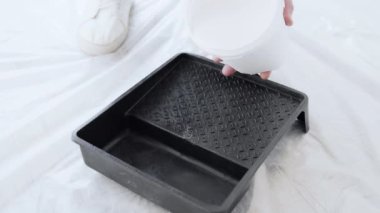 Bir kişi boya tepsisine beyaz boya dökerek kapalı alan boyama projesine hazırlanıyor. Etraftaki sızıntılara ve sıçramalara karşı korunuyor..