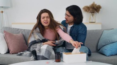 Battaniyeye sarılmış bir kadın iyi görünmezken, partneri kanepede yanında destek sunarak soğuk bir kış günü sıcak bir atmosfer yaratıyor..