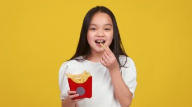 Asyalı genç kız elinde bir karton patates kızartması tutarken gülümsüyor..