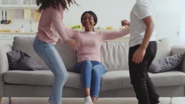 Neşeli bir Afrikalı Amerikalı anne sıcak bir anı iki çocuğuyla paylaşıyor rahat oturma odalarındaki kanepede dinleniyorlar, rahat bir ortamda birbirlerine eşlik ediyorlar..