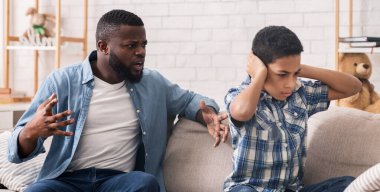 Yetiştirme zorluğu. Kulaklarını tıkayan küçük afro çocuk kızgın babaların evde kanepede oturup azarlamalarını dinlemiyor.