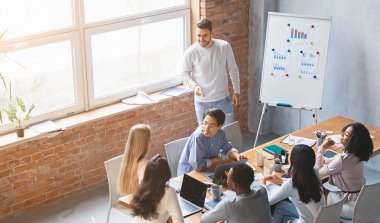 Genç yaratıcı iş adamları sabah saatlerinde çatı katındaki toplantı sırasında pazarlama raporlarını dinliyor.