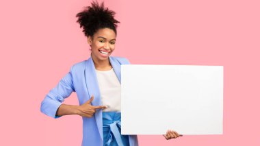 Metin için yer. Beyaz reklam panosunu işaret eden mutlu siyah kadın pembe duvarın üzerinde izole edilmiş.