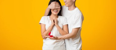 Nişan, romantik konsept. Kız arkadaşının gözlerini kapayan Asyalı genç adam güzel bir yüzük ve turuncu arka planla evlenme teklif ediyor.