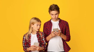 Gadget nesiller. Meraklı küçük kız kardeşi, ağabeyinin akıllı telefonuna bakıp sarı arka planda, boş alanda yan yana dikiliyor.