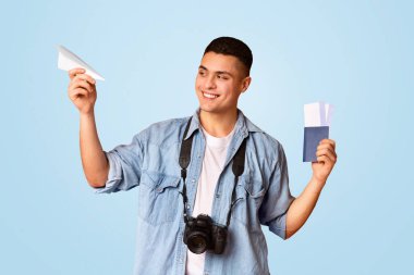 Elinde pasaport, uçuş bileti, kağıt uçak ve turuncu arka plan olan oyuncu bir gezgin.