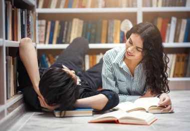 Romance Concept. Two multiracial students doing homework, lying on the floor in library, sharing romantic moment