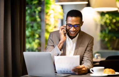 İş, Teknoloji ve İletişim Konsepti. Afro yönetici grafiklerle belgeye bakarken telefon görüşmesi yapıyor