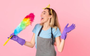 Ev temizliği ve eğlence. Önlüklü ve lastik eldivenli mutlu ev hanımı çok renkli çalılıklarda şarkı söylüyor.