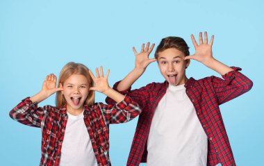 Siblings Fooling. Little brother and sister grimacing at camera, showing funny faces with their tongues out, standing over blue background in studio