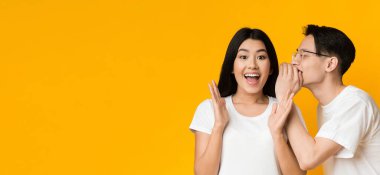 Asyalı bir adam kız arkadaşının kulağına dedikodu fısıldıyor, sarı stüdyo geçmişi var.