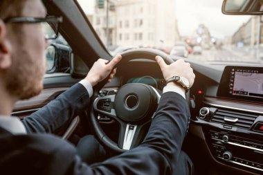 Gözlüklü başarılı iş adamının şehir merkezindeki işinden eve dönüşünün arka görüntüsü, direksiyondaki eller