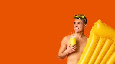 Yaz tatili kavramı. Dalış maskesi ve şişme yatağı olan, turuncu stüdyo arka planında kokteyl içen, boş alana bakan, panorama