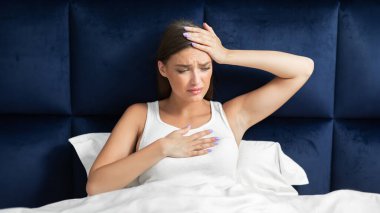 Coranavirus Hastalığı. Hasta kadın ateşleniyor ve nefes almakta zorlanıyor. Başa dokunmakta zorlanıyor. Evde yatakta oturuyor..