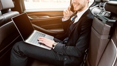 Her zaman müsaidim. Takım elbiseli, gülümseyen erkek CEO, boş ekranlı dizüstü bilgisayar kullanıyor telefonda konuşuyor, kopyalama alanı, yan görünüm.