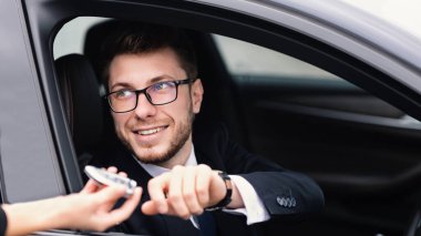 Test sürüşü yeni araba. Gözlüklü genç işadamı kadın elinden araba anahtarı alıyor, sürücü koltuğunda oturuyor.