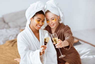 Evde cilt bakımı yaparken şampanya ile kadeh kaldırırken göz bandı takan çok ırklı mutlu sevgililer.