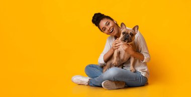 Evcil hayvanlar ve insanlar. Güzel Afro Kadın Ger Şirin Köpeğiyle Poz Veriyor, Stüdyoda Sarı Arkaplanda Oturuyor, Boşluğu Kopyala
