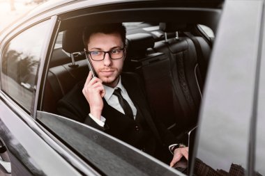 Her zaman müsaidim. Takım elbiseli ve gözlüklü bir erkek taksi durağında oturmuş, camdan dışarı bakıyor.