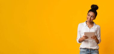 Elinde dijital tabletle ilgilenen siyah kadın sarı arkaplan ve panorama üzerindeki kopya alanına bakıyor.