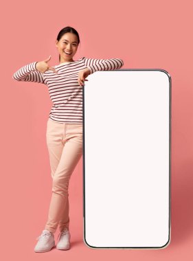 Büyük beyaz ekranlı akıllı telefona eğilip işaret eden, uygulamanız veya web siteniz için kopyalama alanı gösteren, Pembe Stüdyo arka planında duran,