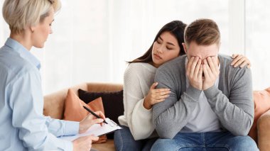 Çift Terapisi Konsepti. Psikoterapi randevusu sırasında psikologların ofisinde oturan ve ağlayan koca rahatlatan eş. Seçici Odaklanma