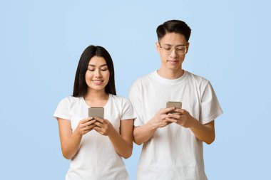 Neşeli Asyalı milenyum çifti cep telefonlarını karıştırıyor, iletişim kuruyor veya arkadaşlarıyla sohbet ediyor, sarı arka plan