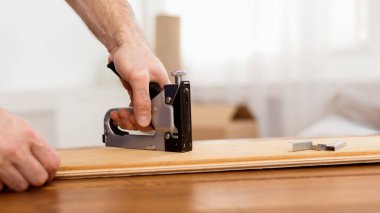 Tanımlanamayan Marangoz, Staple Gun Aletini kullanarak mobilya yapıyor ve içeride ahşap tahtayla çalışıyor. Marangozluk ve Mobilya Toplama Hizmetleri Reklam Konsepti. Kırpılmış Vuruş, Panorama