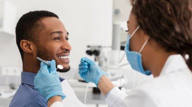 Genç Afrikalı adam modern klinikte tedavi görürken dişçisine gülümsüyor.