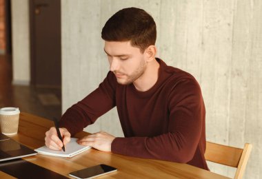 Modern ofiste masa başında oturan ve not alan genç bir çalışan. Seçici Odaklanma