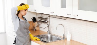 Ev Hayatı Konsepti. Önlüklü yorgun bir kadın mutfakta durmuş, lavabodaki kirli tabaklara bakıyor, boşluğu kopyalıyor.