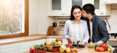 Aşk Konsepti. Mutlu çift sağlıklı salata pişiriyor, kız sebze doğruyor, erkek kadını öpüyor.