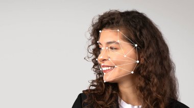 Kıvırcık saçlı genç bir kadın gülümserken yüzünde yüz tanıma işaretleri görülüyor. Teknoloji modern bir ortamda anahtar yüz özelliklerini vurguluyor.