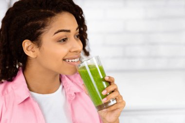 Detox konsepti. Elinde ev yapımı yeşil meyve suyu olan, boş alana bakan siyah bir kızın portresi.