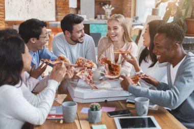 Ofis yemeği servisi. Öğle yemeği saatinde ofiste pizza yiyen mutlu çok ırklı genç işçiler grubu.