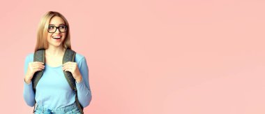 Sırt çantası ve gözlük takan mutlu kız öğrencinin portresi pembe stüdyo duvarından izole edilmiş kopyalama alanına bakıyor.