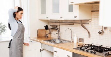 Yine temizlik. Mutfak odasında durmuş mobilyalara bakan yorgun ve stresli genç bir kadın.