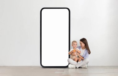 Parlak, modern bir odada, bir anne elinde portakallı atıştırmalık tutan küçük çocuğunun yanında yere oturur. Büyük boş bir ekranın önündeler, sakin bir atmosfer yaratıyorlar..