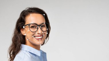 Gözlüklü bir kadın gülümserken teknoloji onun yüz hatlarını yakalıyor. İyi ışıklandırılmış bir stüdyoda yüz tanıma becerilerindeki gelişmeleri gösteriyor..