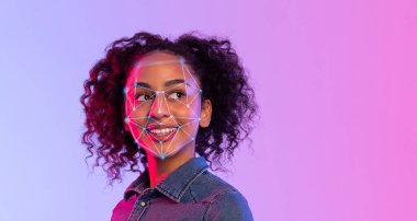 Kıvırcık saçlı Afrikalı Amerikalı genç bir kadın renkli ışıklarla aydınlatılmış modern bir iç mekan ortamında yüz tanıma teknolojisi testine katılırken kendinden emin bir şekilde gülümsüyor..