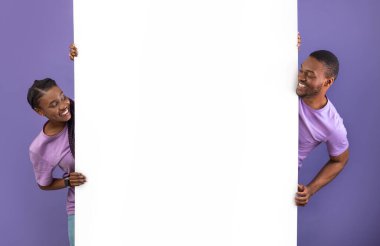 Gülümseyen genç siyahi insanlar ellerinde beyaz dikey reklam panosu tutuyorlar, metin ve tasarımın için bedava fotokopi alanı sunuyorlar, olumlu adam ve bayan pankarttan dışarı bakıyor, mor menekşe arka plan duvarı.