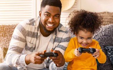 Gülümseyen Afrikalı Amerikalı baba ve kızı koronavirüs karantinası sırasında bilgisayar oyunu oynuyorlar.
