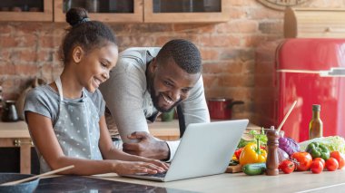 Gülümseyen afrikalı baba ve kızı güzel tarifi arıyor, mutfakta dizüstü bilgisayar kullanarak, boş alan