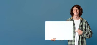 Neşeli milenyum çocuğu turkuaz arka plandaki boş postere işaret ediyor. Tasarımın için yer var.