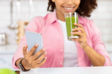 Kaloriler hesaplanıyor. Siyah kız akıllı telefon kullanıyor ve mutfakta ev yapımı smoothie içiyor.