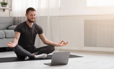 Karantinada sakin olun. Millennial elemanı antrenörle internetten laptopla meditasyon yapıyor. Boş alan.