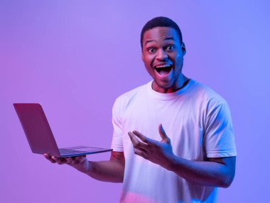 Güzel web sitesi. Heyecanlı Siyah Adam 'ın portresi, dizüstü bilgisayarı Neon Işıklandırma Altında, aşırı mutlu Afrikalı Amerikalı Adam laptopla başarıyı kutluyor, Mor Stüdyo Arkaplanı' nın başında duruyor,
