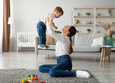 Koşulsuz sevgi. Genç ve mutlu bir anne, sevimli oğluyla evde vakit geçiriyor, onu havaya kaldırıyor, çocuk ile oturma odasında oynuyor, bedava uzay...