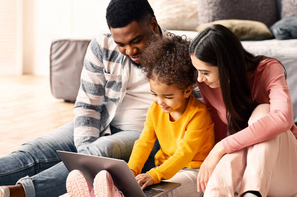 Little girl is typing at laptop, international parents help her